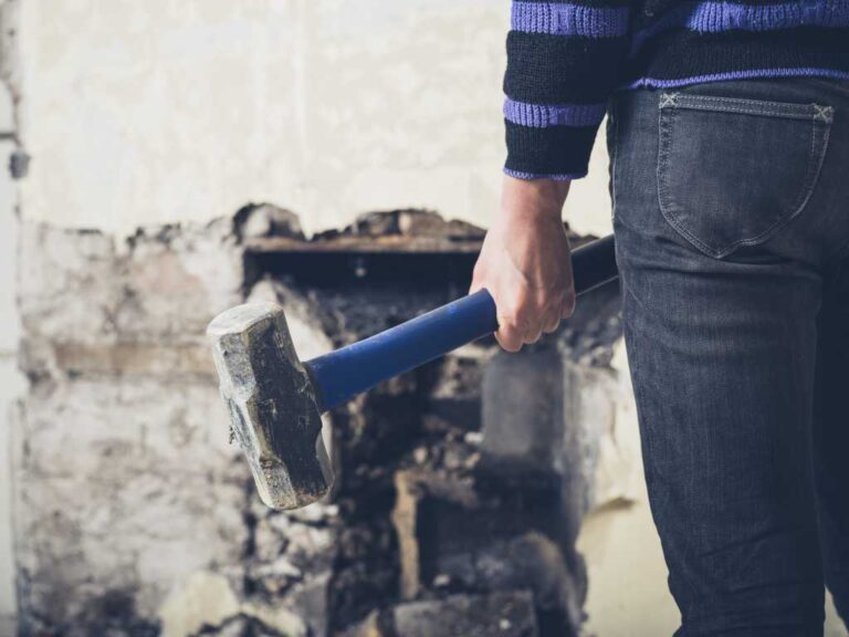A young woman is opening up an old fireplace in a Victorian house with a sledge hammer